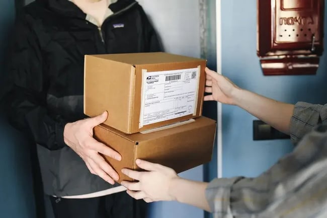 Primer plano de manos intercambiando cajas de cartón en interiores, simbolizando un servicio de entrega
